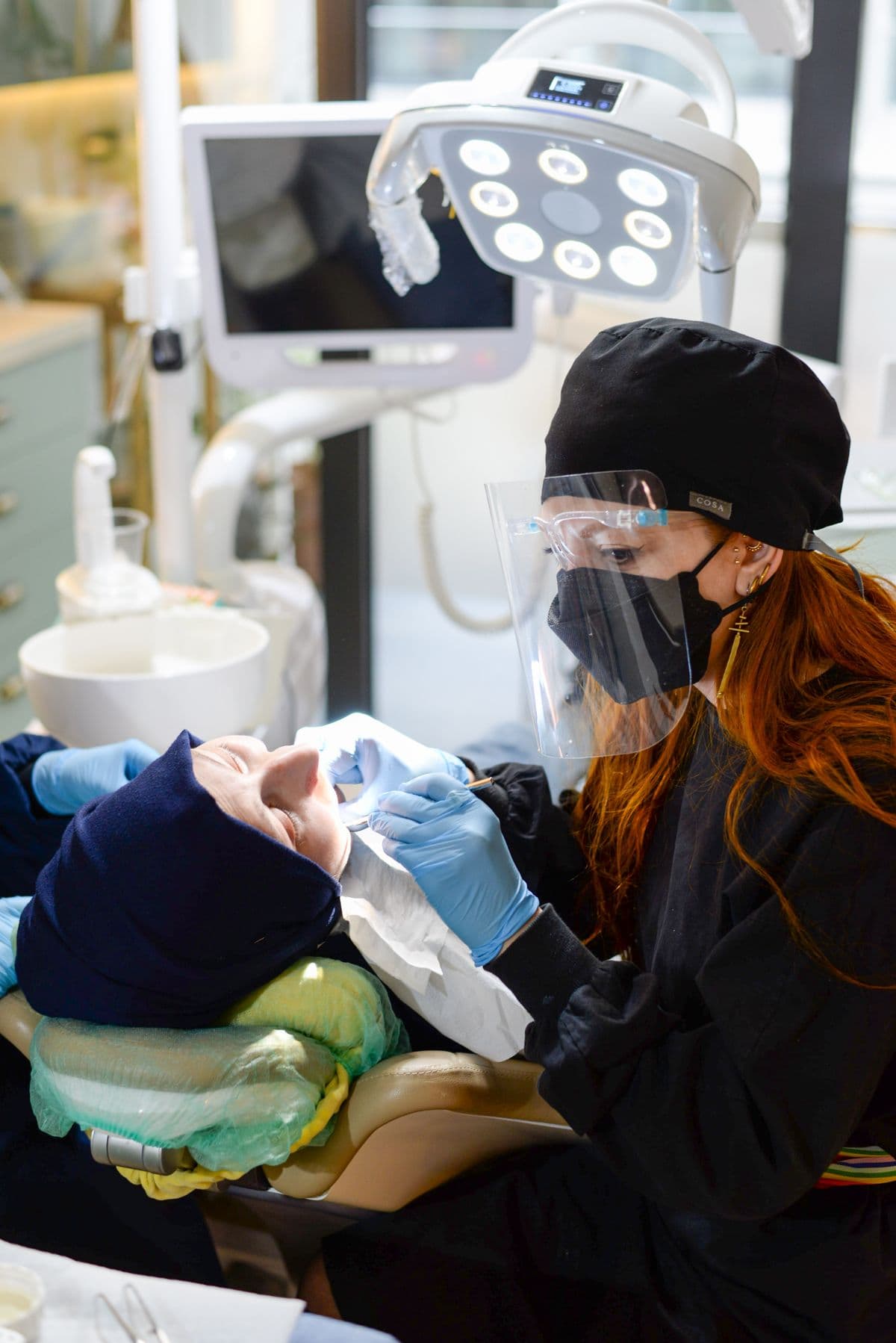 A dental clinician in a face shield and gloves treating a patient reclining in the dental chair