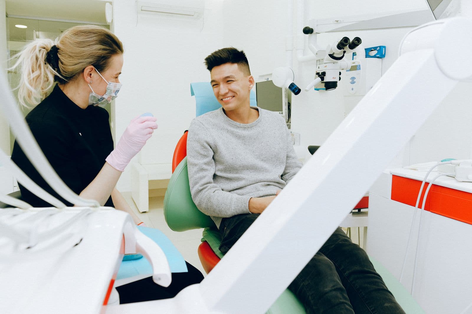 A smiling patient talking with a masked dental professional in a bright modern dental clinic